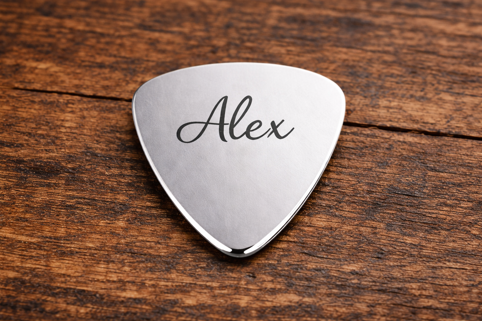 Silver guitar pick with 'Alex' engraved on a wooden surface