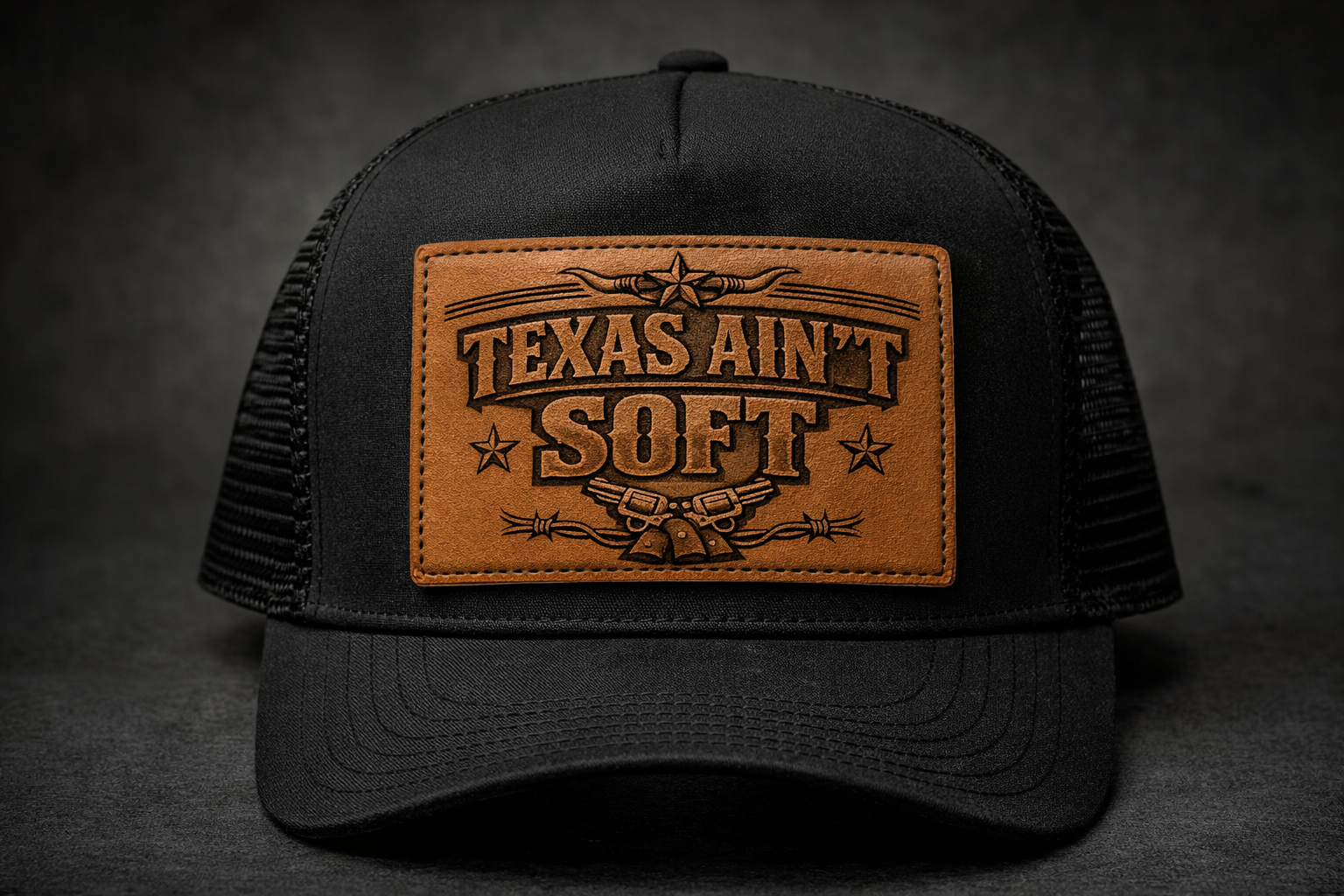Black trucker cap with a brown leather patch reading 'Texas Ain't Soft' on a dark background