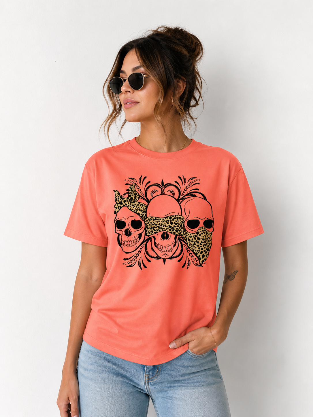 Woman wearing a coral t-shirt with skull designs on a plain background