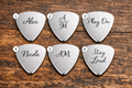 Six silver guitar picks with engraved names on a wooden surface
