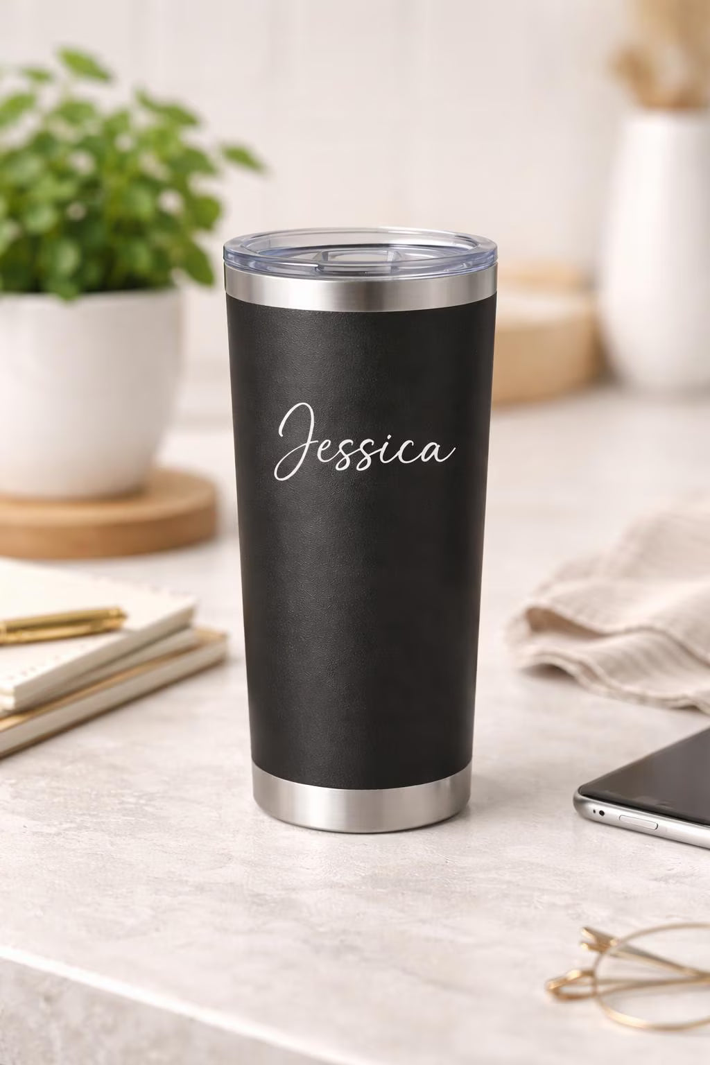 Black tumbler with 'Jessica' engraving on a light surface with a plant and phone in the background