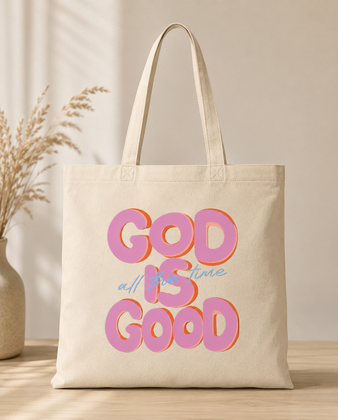 Beige tote bag with 'God is Good' text in colorful letters on a neutral background